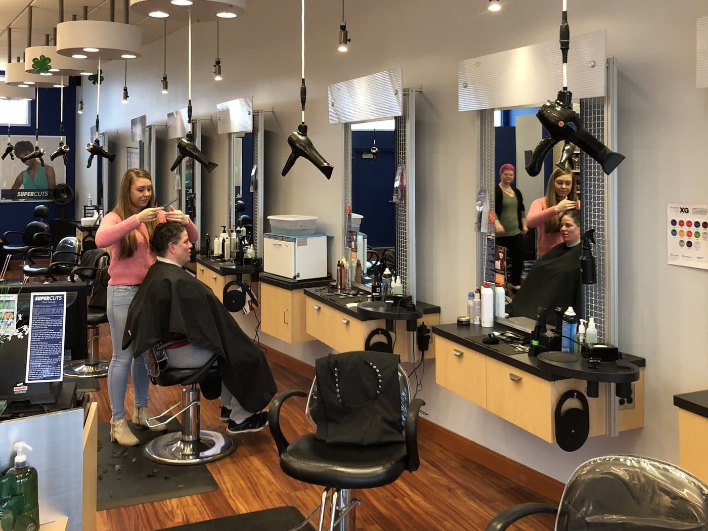 Two MjjM stylists cutting caped clients at mirrored styling stations under warm pendant lights