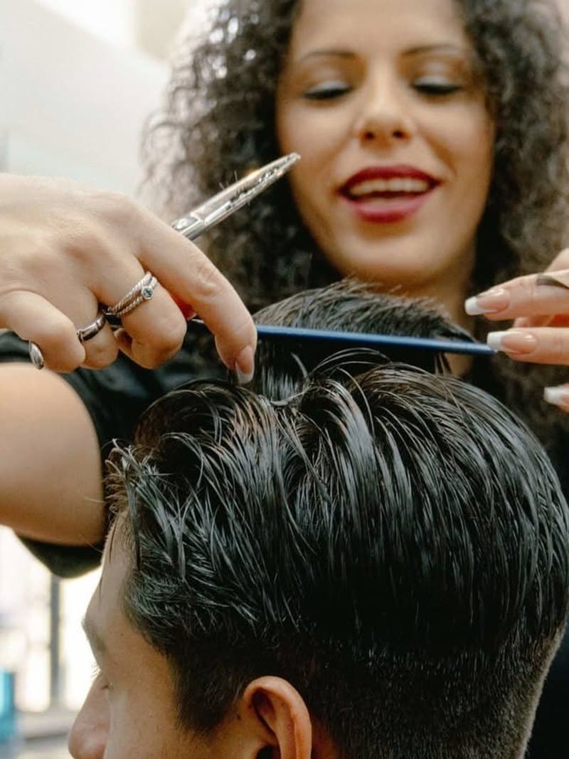 Close-up of a stylist's hands working scissors and a comb through a client's dark hair